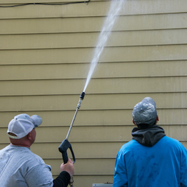 professionals washing siding of home with sprayer