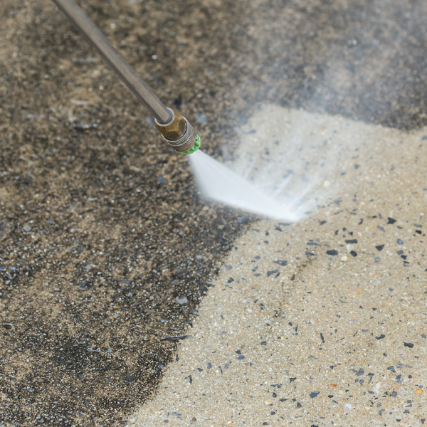 a pressure washer to clean a driveway, with water spraying out of the nozzle and creating a mist in the air