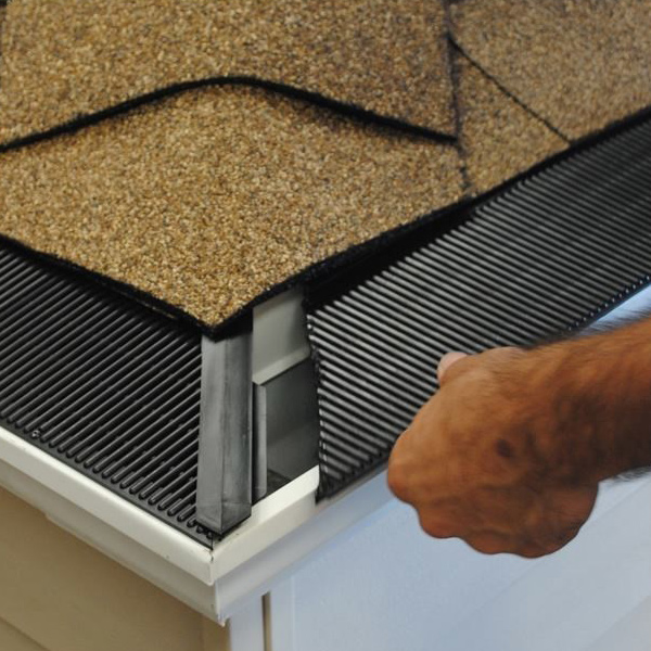 a person's hand installing a raindrop-shaped gutter guard onto a white gutter